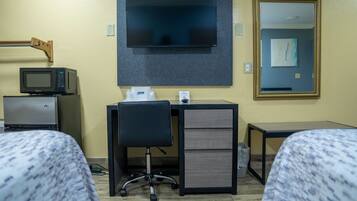 A hotel room with a television mounted on the wall, a desk with a computer, a chair, and two beds.