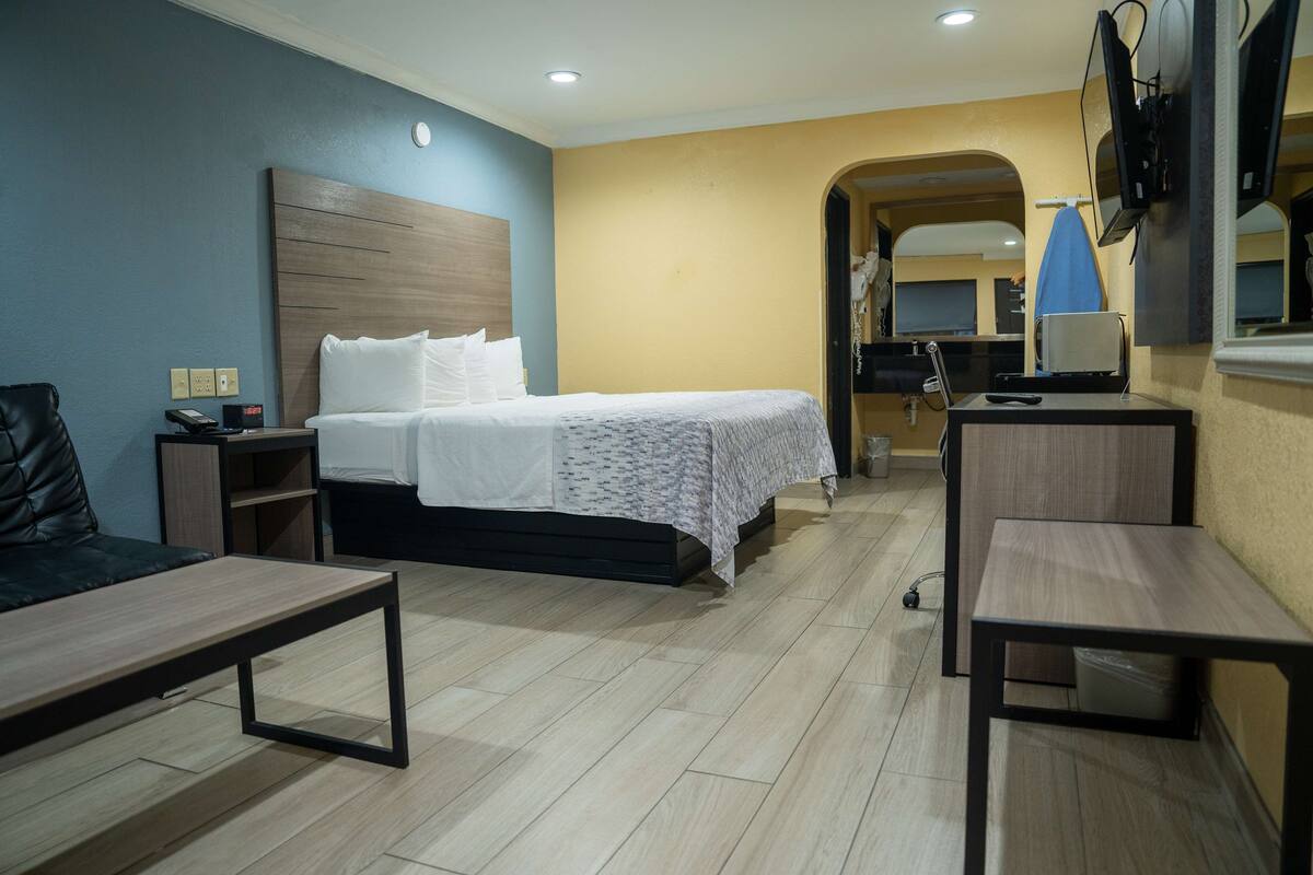 Habitación de hotel con cama, escritorio, silla, televisión y baño visible a través de un arco.
