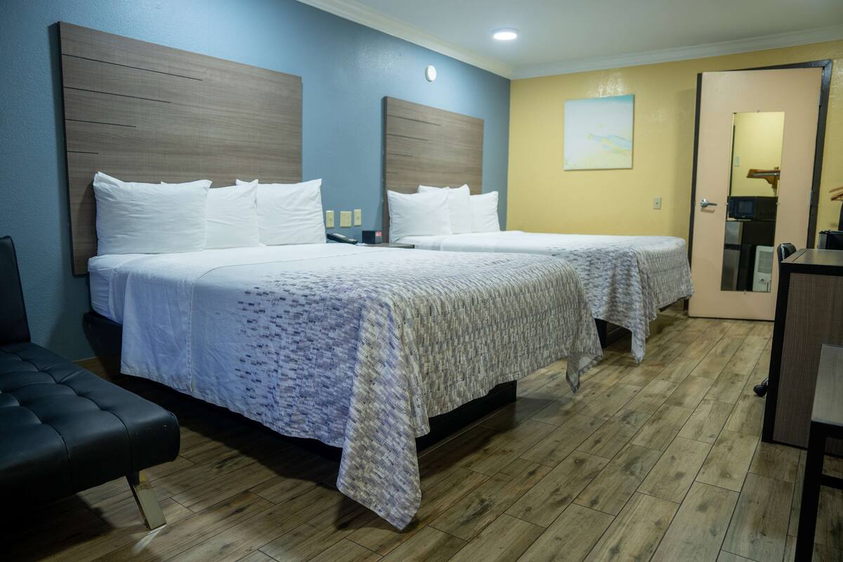 Habitación de hotel con dos camas, un banco, un escritorio y un espejo.