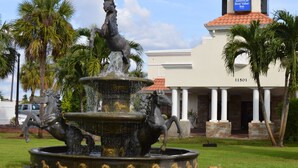 A fountain with horse statues in front of a building with columns and a red-tiled roof. - Americas Best Value Inn Ft. Myers (Fort Myers)