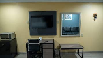 A hotel room with a flat-screen TV mounted on the wall, a small desk with a chair, a microwave, and a refrigerator.