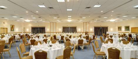 A large banquet hall with round tables and chairs, arranged in rows.