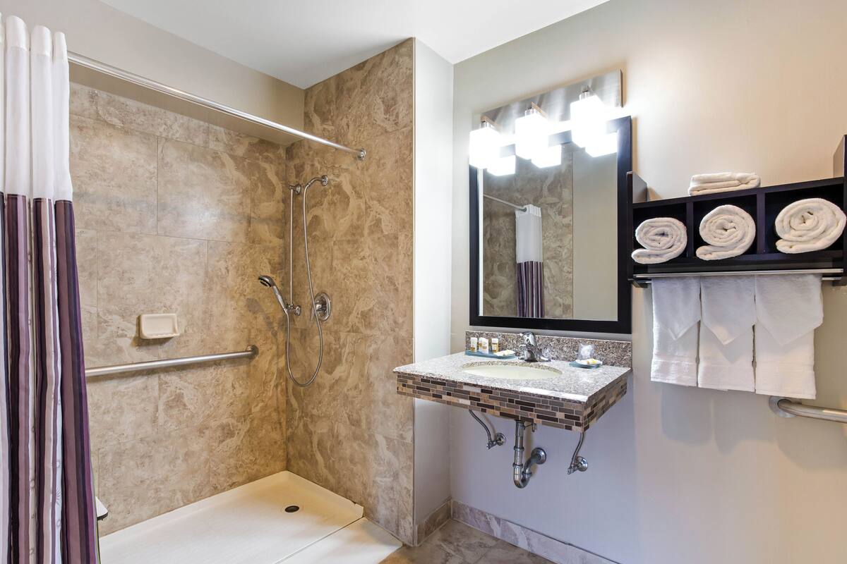 Un baño con ducha, lavabo con espejo y un perchero para toallas.