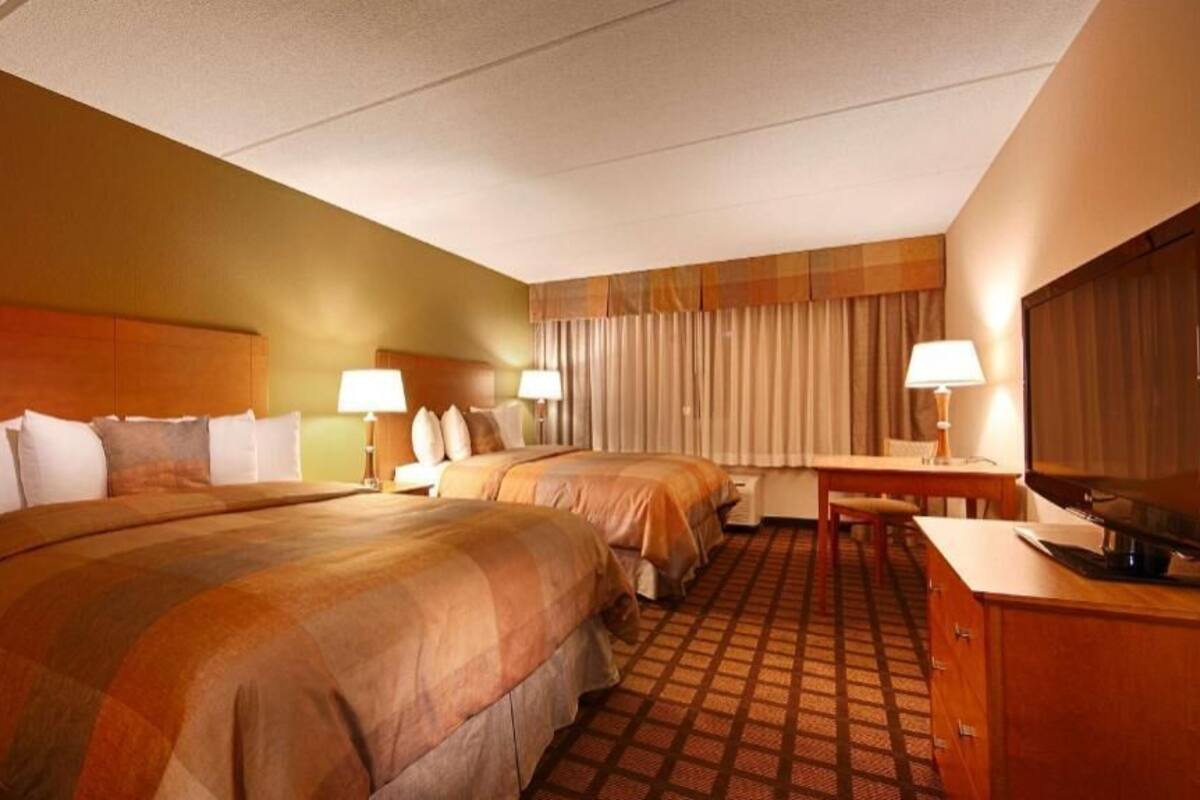 Una habitación de hotel con dos camas, un escritorio, un televisor y una ventana con cortinas.