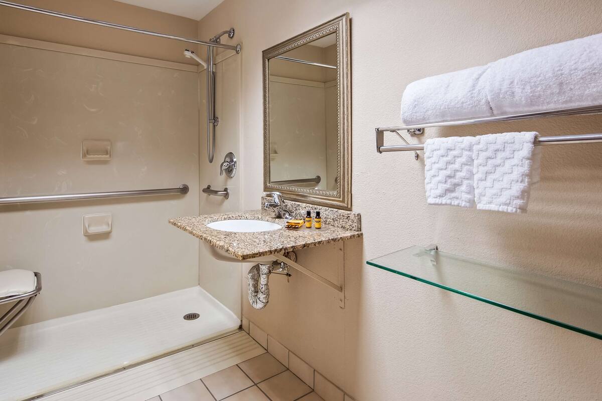 Un baño con cabina de ducha de vidrio, un lavabo con encimera de granito, un espejo y un perchero con dos toallas.