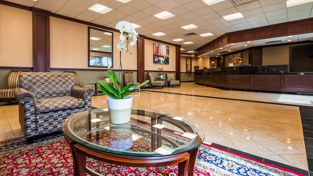 Un vestíbulo con mostrador de recepción, sofás estampados, una mesa con superficie de vidrio y una planta en maceta, y un espejo decorativo.