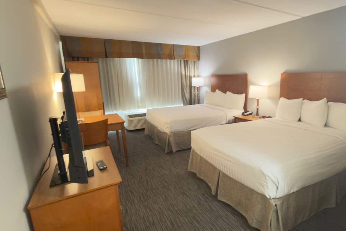 Habitación de hotel con dos camas, un escritorio, una silla, una lámpara y un ventanal con cortinas.