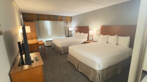 A hotel room with two beds, a desk, a chair, a lamp, and a window with curtains.