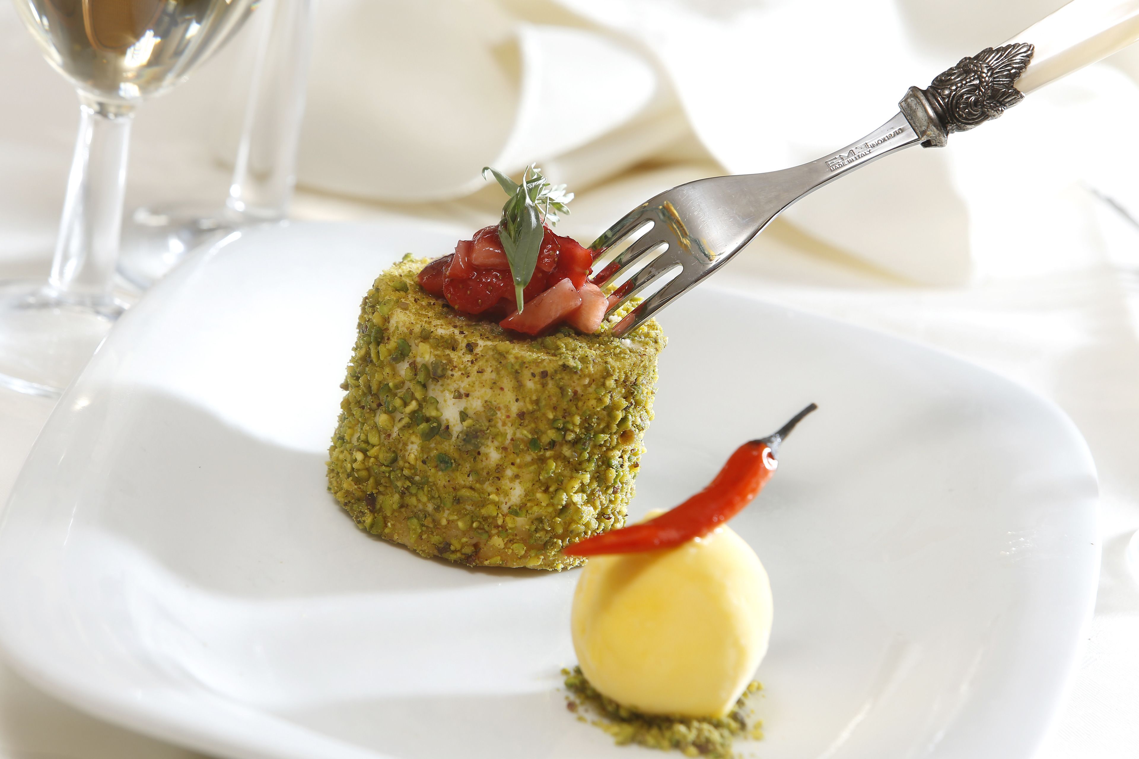 A dessert on a white plate with a fork and a red chili pepper.