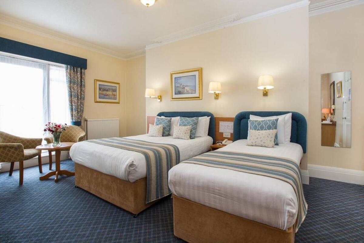 A hotel room with two beds, a sitting area with a chair, a small table, and a window with curtains.
