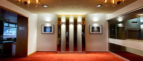A spacious room with a red carpet, two chandeliers, and a mirrored wall.