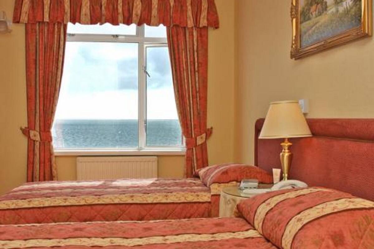 A hotel room with two beds, a window with curtains, a painting on the wall, and a lamp on a bedside table.
