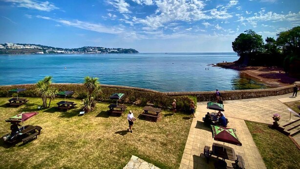 A coastal view with a grassy area, picnic tables, and umbrellas. - Livermead Cliff Hotel (Torquay)