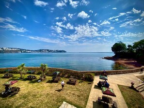 A coastal view with a grassy area, picnic tables, and umbrellas. - Livermead Cliff Hotel (Torquay)