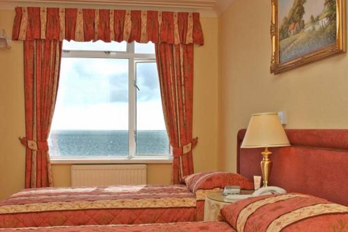 A hotel room with two beds, a window with curtains, a painting on the wall, and a bedside lamp.