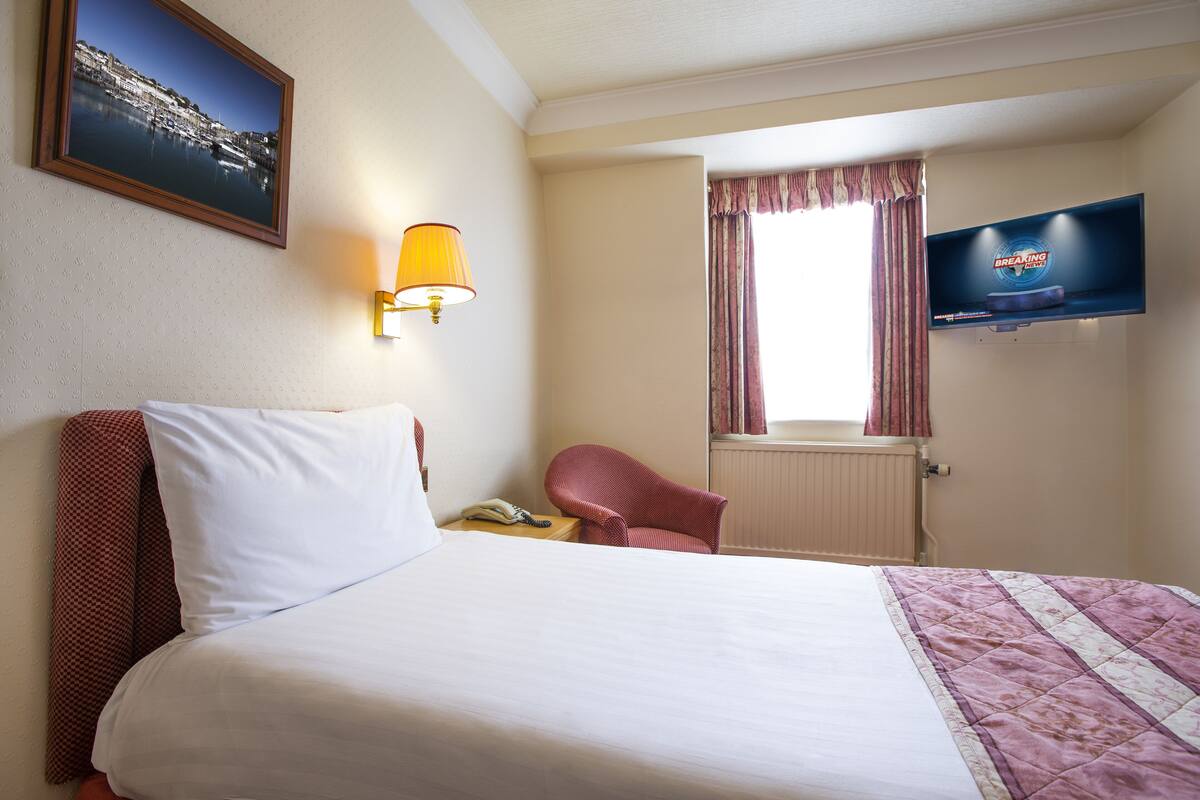 A hotel room with a bed, a chair, a TV, a lamp, and a window with curtains.