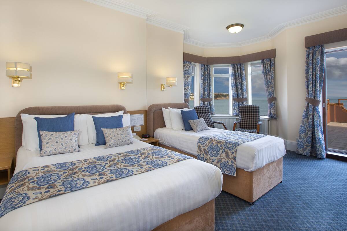 A hotel room with two beds, a view of the sea, and a balcony with a chair.