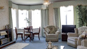 A traditional living room with a fireplace, a television, and a dining area. - Livermead Cliff Hotel (Torquay)
