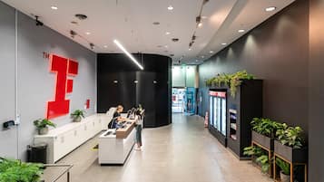 A modern reception area with a prominent red logo, a counter, and potted plants.