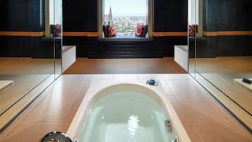 A modern bathroom with a large bathtub, a window with a city view, and a bench with cushions.