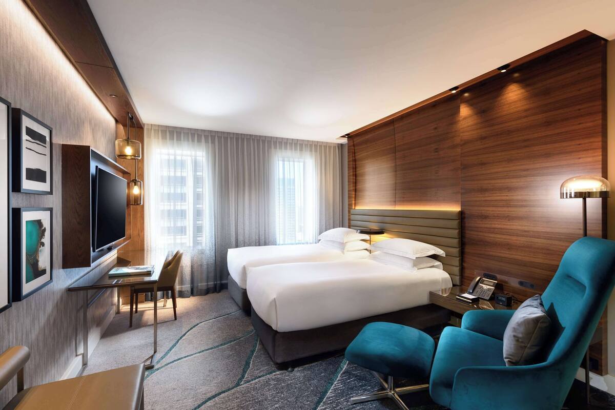 A hotel room with a large bed, a desk with a chair, a TV, and a seating area with a chair and ottoman.