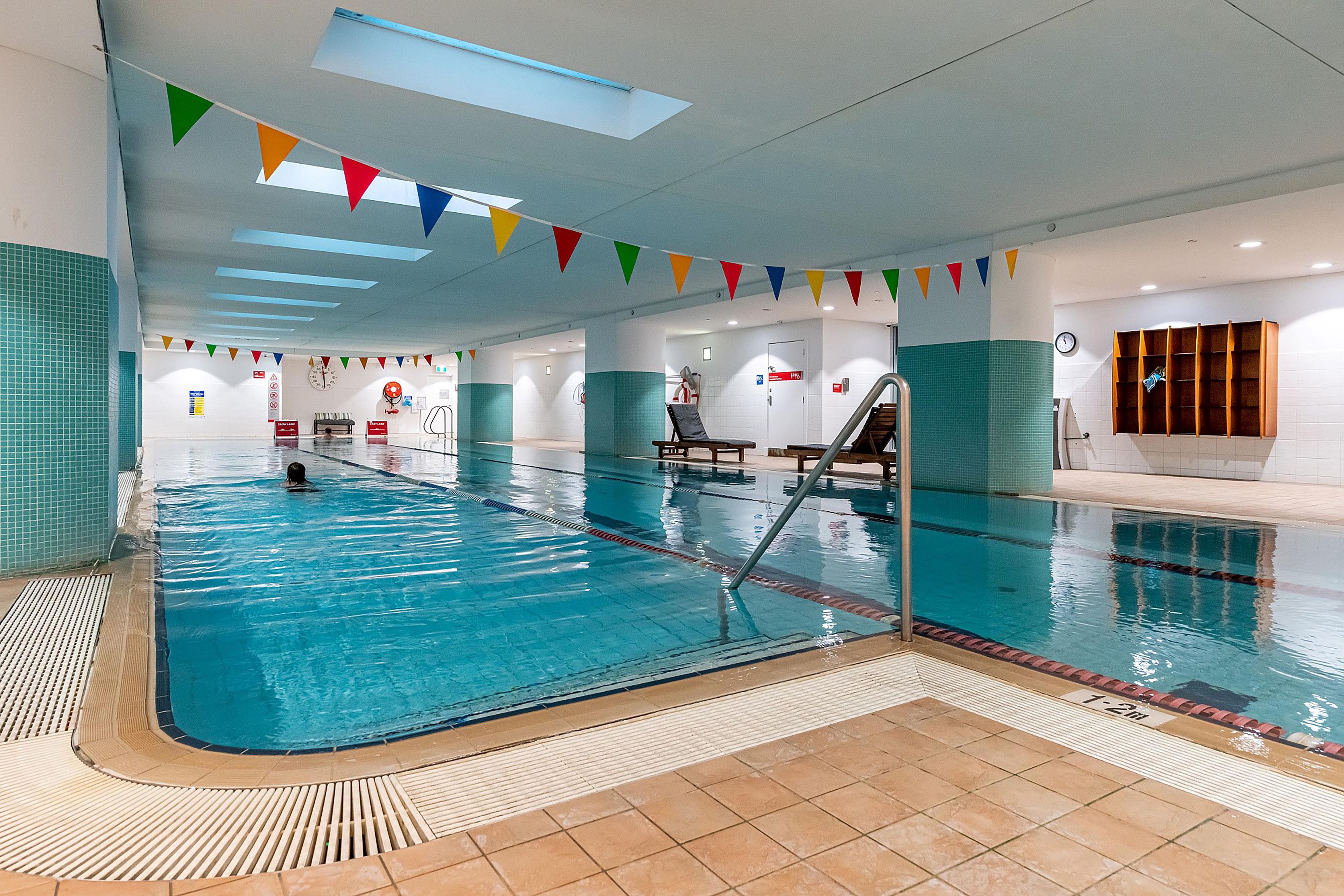 An indoor swimming pool with clear lanes, a lifeguard chair, and a clock on the wall.