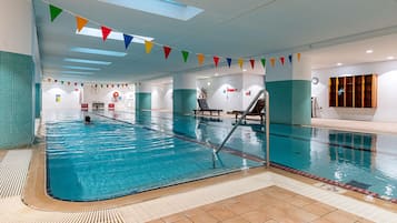 An indoor swimming pool with clear lanes, a lifeguard chair, and a clock on the wall.