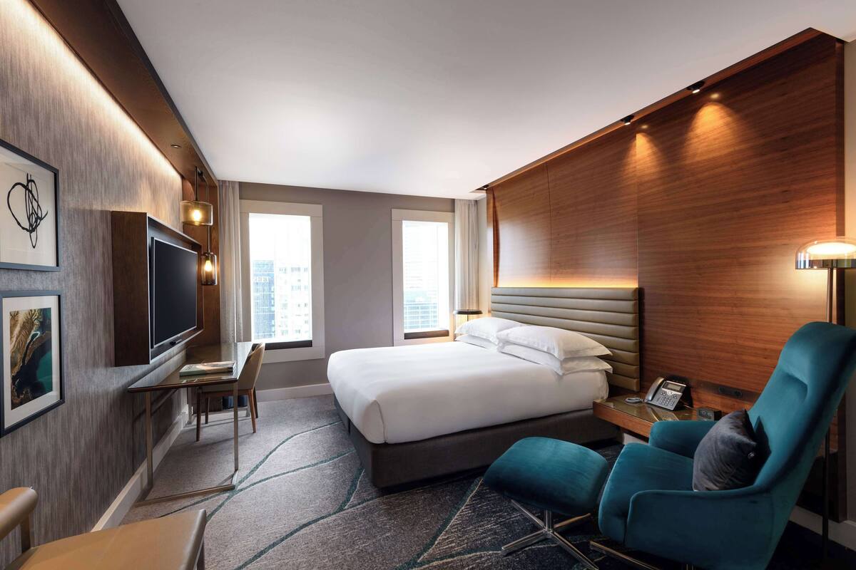 A modern hotel room with a large bed, a desk, a TV, and a seating area.