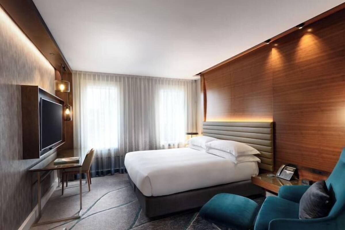 A modern hotel room with a bed, a TV, a desk, and a chair.