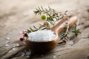 A wooden spoon filled with salt and sprigs of rosemary on a wooden surface.