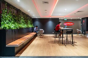 A modern lounge area with a long bench, a bar area with stools, and a wall of green plants.