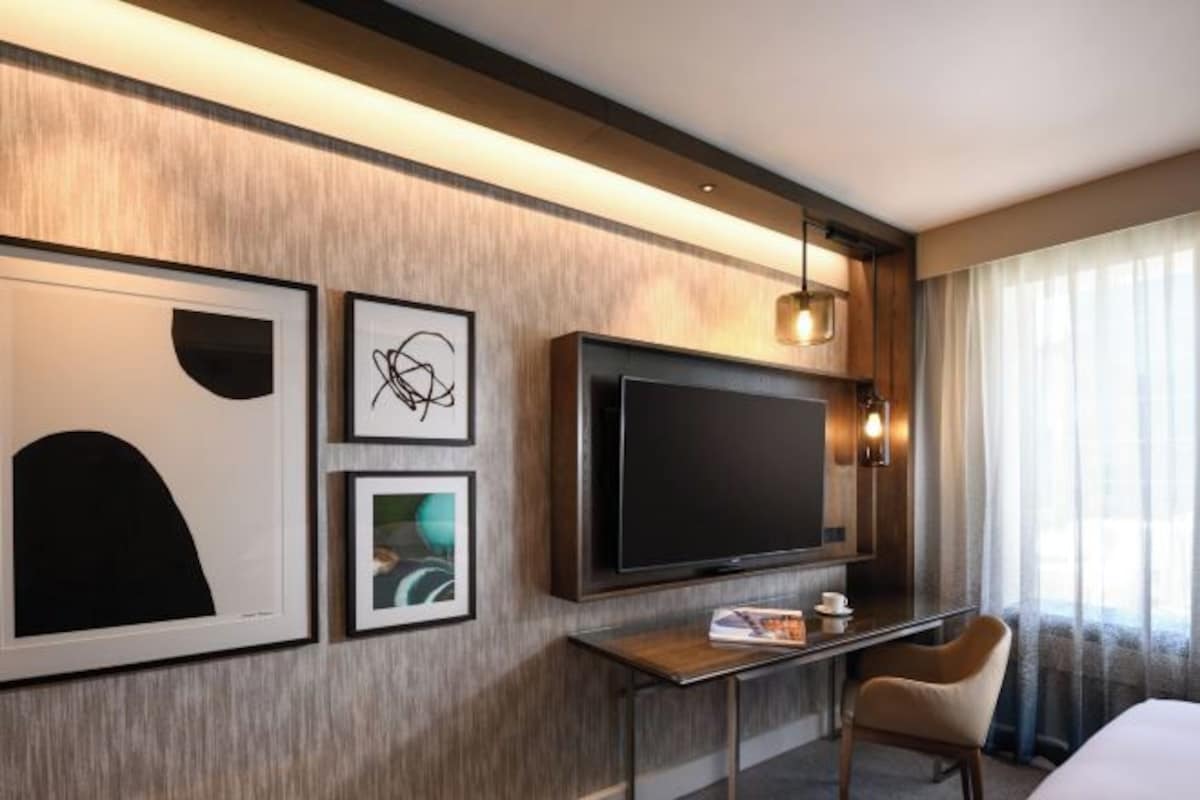 A hotel room with a large flat-screen TV, a desk with a chair, and artwork on the wall.