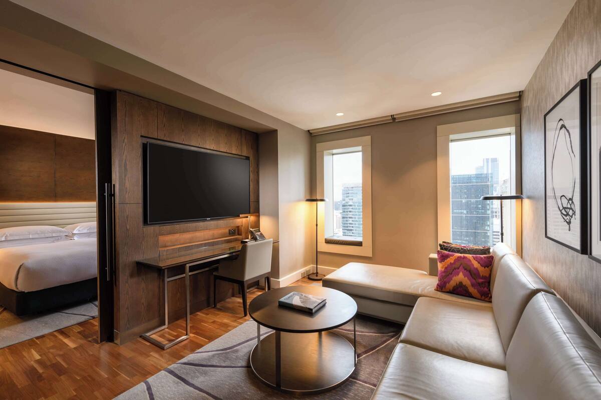 A modern hotel room with a bed, a flat-screen TV, a sofa, and a small table.