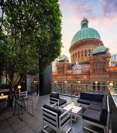 An outdoor seating area with tables and chairs, a large tree, and a historic building with a dome in the background.