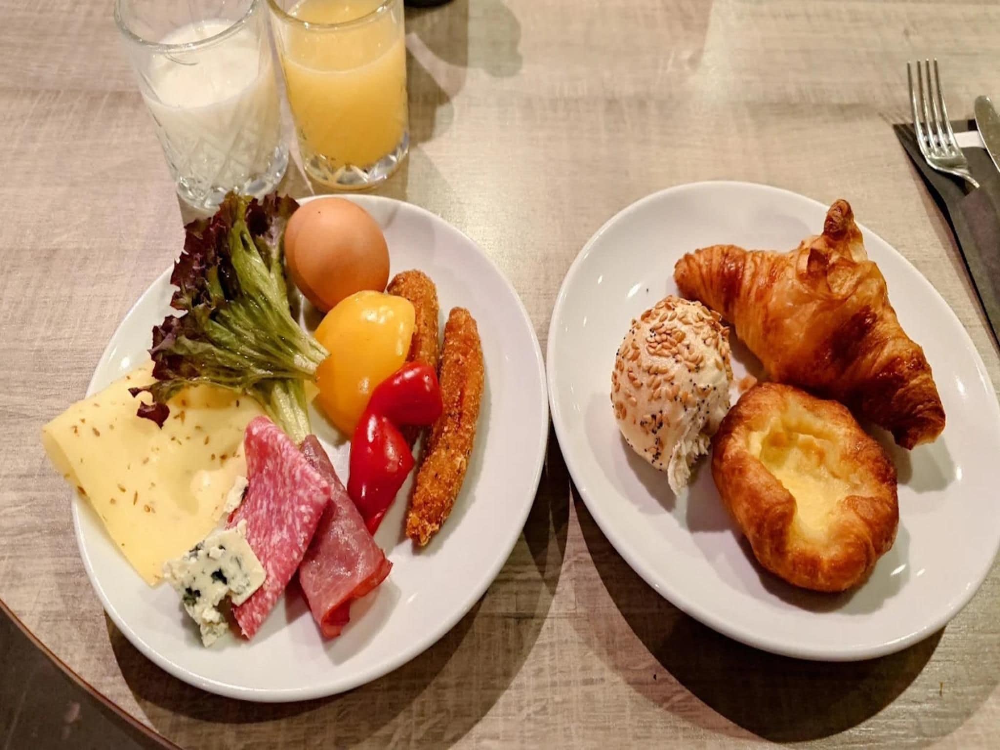 Dos platos de comida, uno con queso, carne y verduras, y el otro con cruasanes y un pastel.