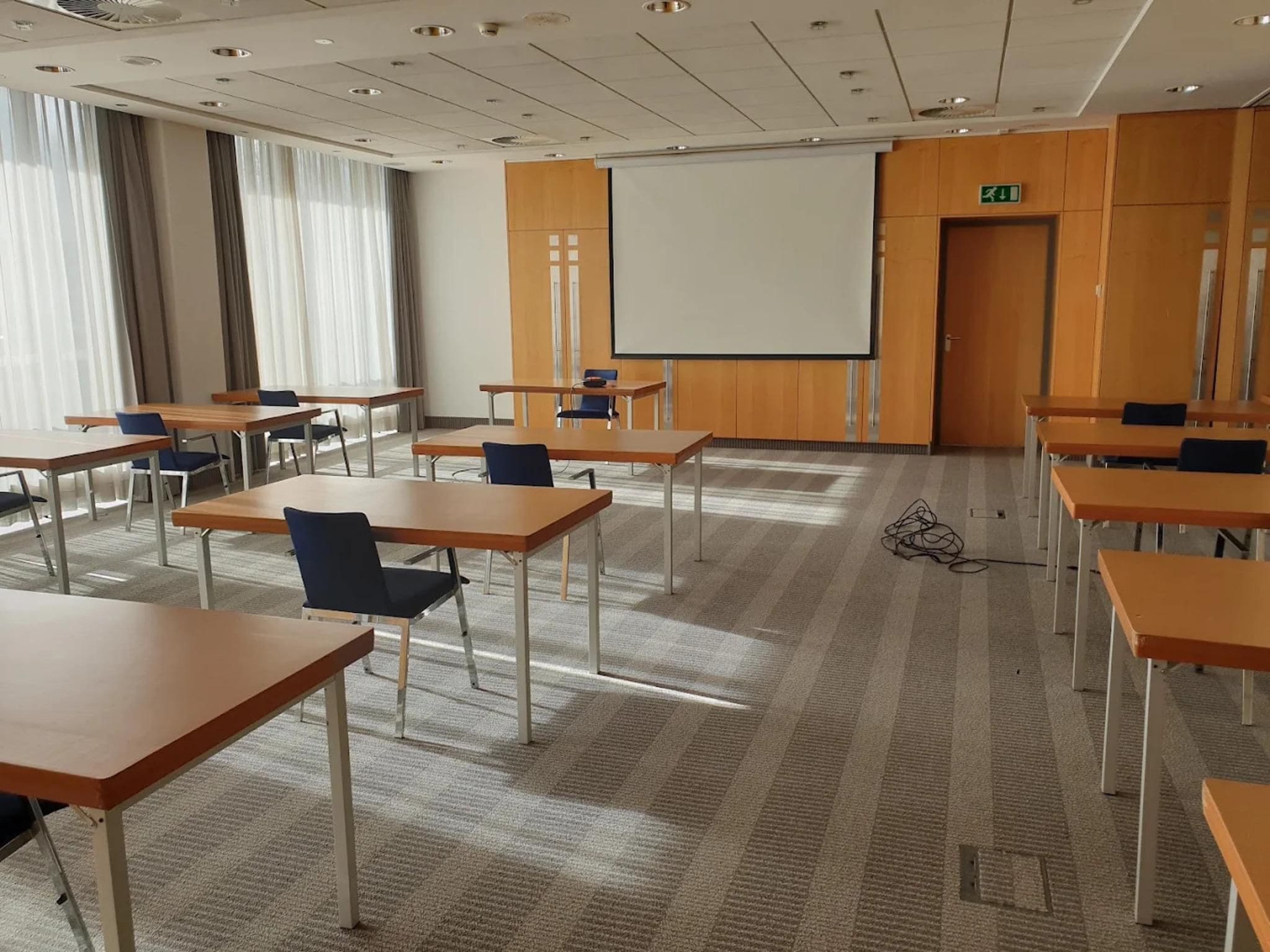 A conference room with multiple tables and chairs, a projector screen, and a carpeted floor.