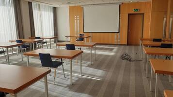 A conference room with multiple tables and chairs, a projector screen, and a carpeted floor.