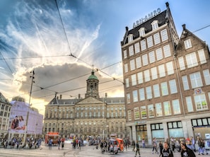 Un edificio histórico con una imponente torre del reloj, una línea de tranvía en la parte superior y una concurrida calle con peatones y vendedores ambulantes.