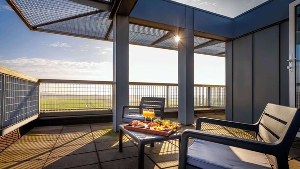 Un balcón con una mesa dispuesta para el desayuno, sillas y vistas a un campo.