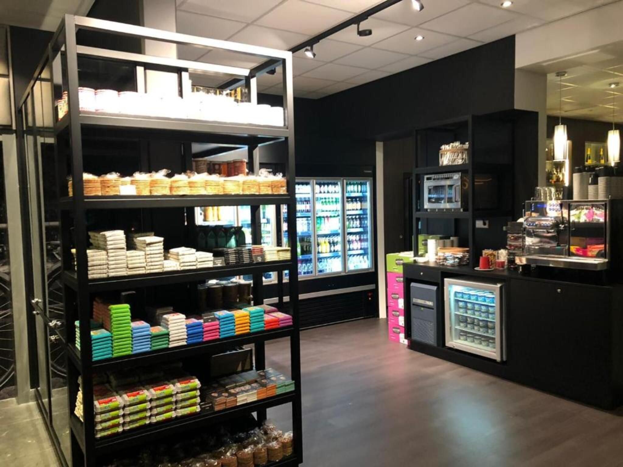 A modern retail space with shelves stocked with various products, a refrigerated display case, and a coffee station.