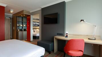 A hotel room with a bed, a desk, a red chair, a TV, and a coffee machine.