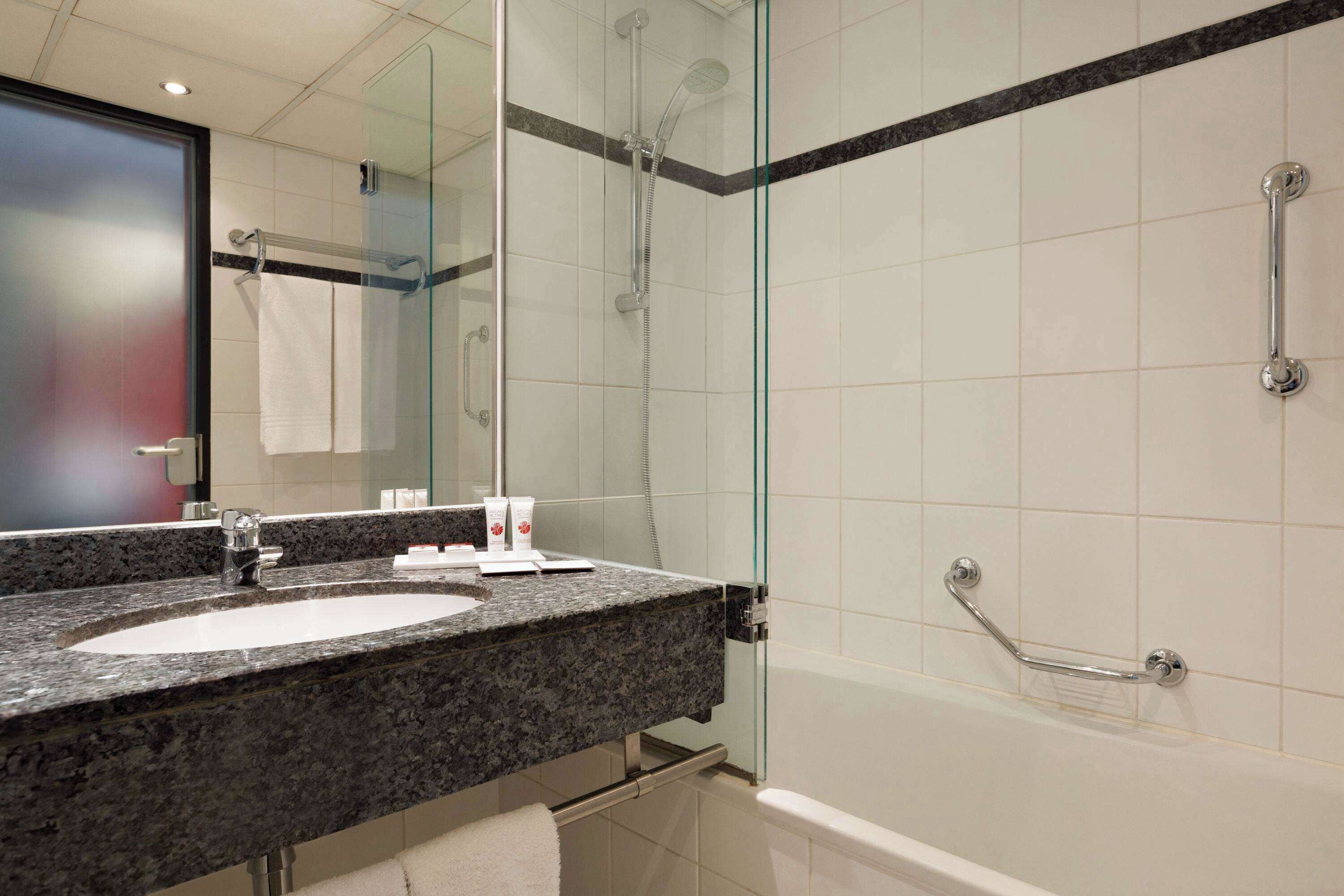 Une salle de bain moderne avec un lavabo sur un plan de travail en granit, une cabine de douche en verre et une douchette à main.