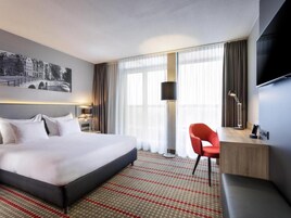 Habitación de hotel con una cama grande, un escritorio, una silla, un televisor y una ventana con cortinas.