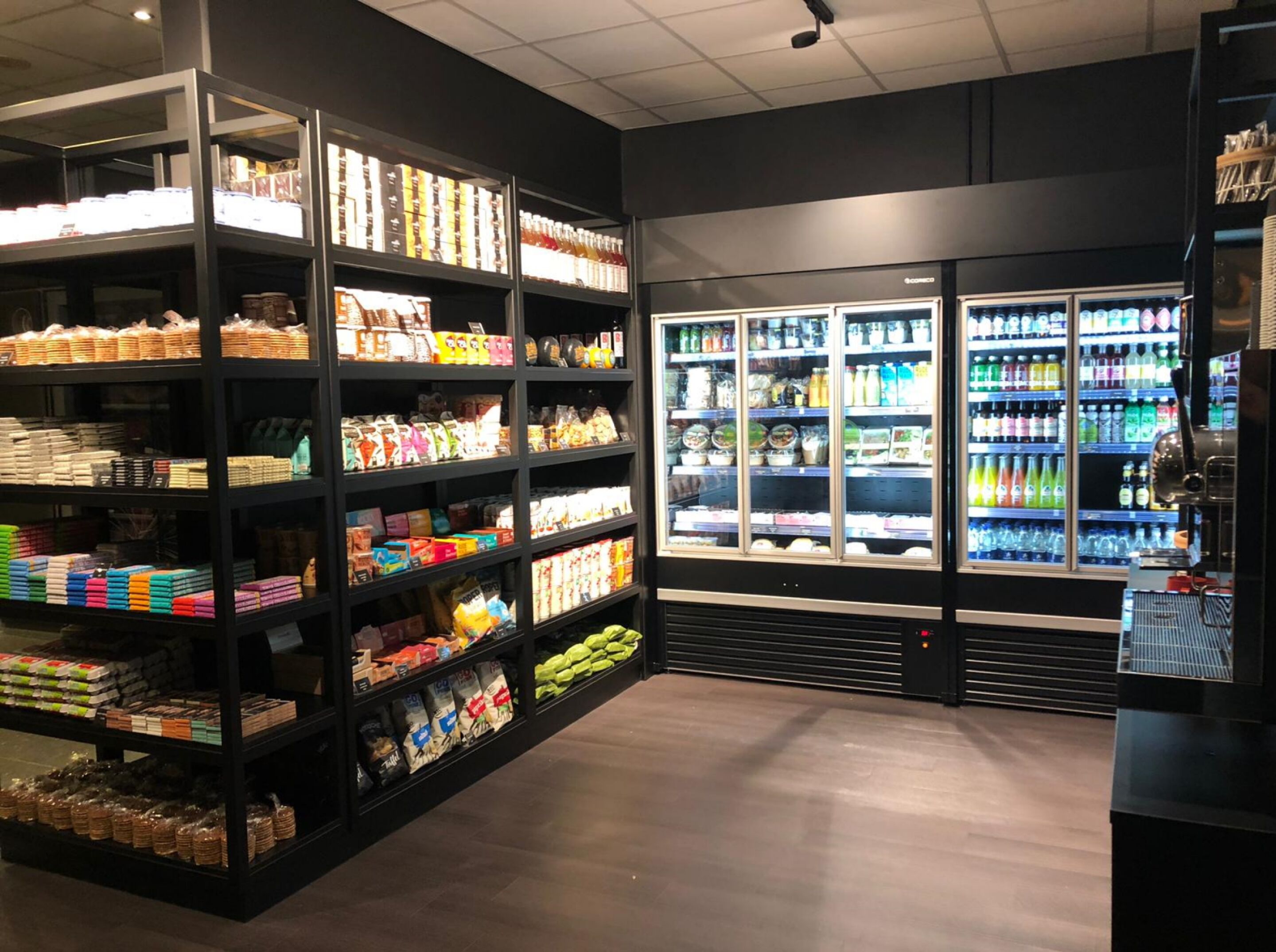 Una tienda de comestibles con estantes llenos de productos variados y una sección refrigerada con bebidas.