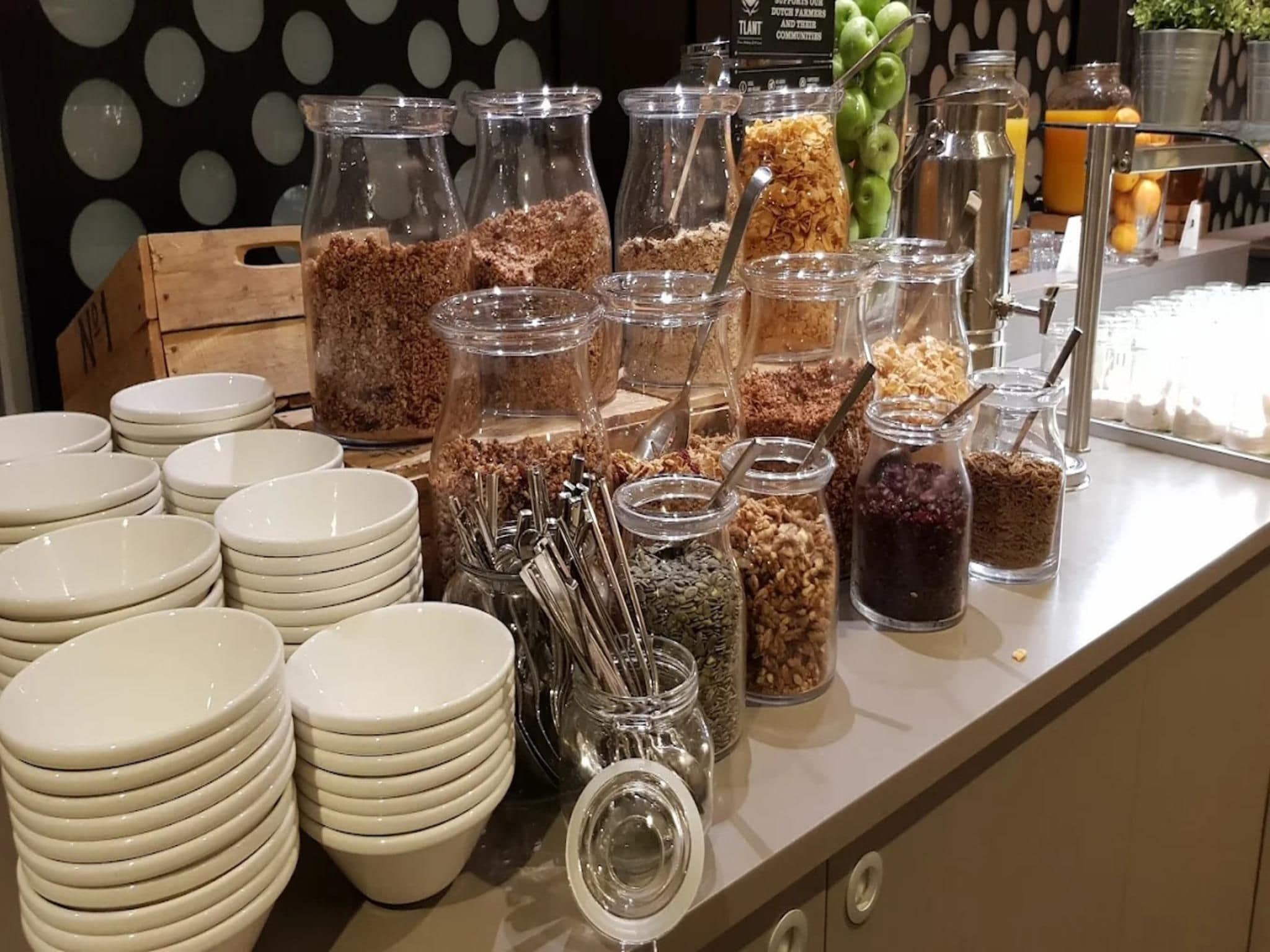 Un buffet avec différents plats présentés dans des bocaux et des piles d’assiettes blanches.