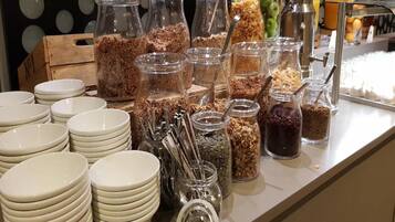 Un buffet avec différents plats présentés dans des bocaux et des piles d’assiettes blanches.