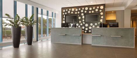 Et moderne receptionområde med et stort vindue, en receptionsdisk og plantekasser.