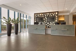 Una zona d'entrada amb un disseny modern, amb un gran finestral, un taulell de recepció i plantes en testos.