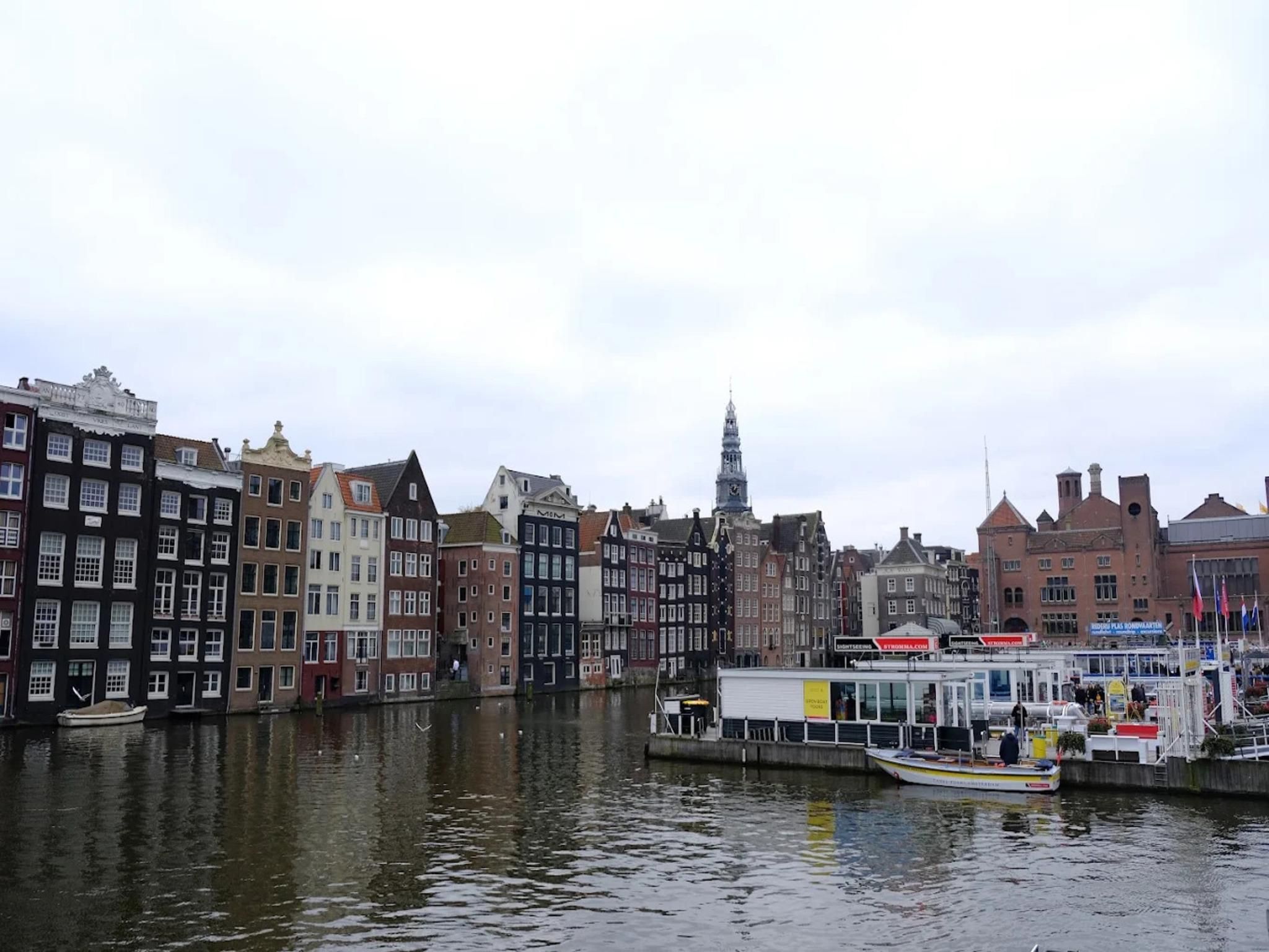 Een gracht met historische gebouwen aan de ene kant en een moderne boot aan de andere kant.