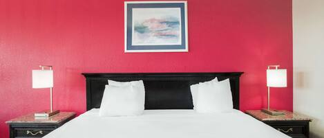 Una habitación de hotel con una cama grande, dos mesitas de noche, una lámpara de noche, un cuadro en la pared y una pared de acento roja.